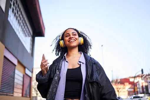 Spotify розлютив передплатників після оголошення про друге підвищення цін на преміум-підписки за рік, що вплинуло на сотні мільйонів користувачів сервісу. Життєрадісна жінка слухає музику з мобільного телефону на вулиці