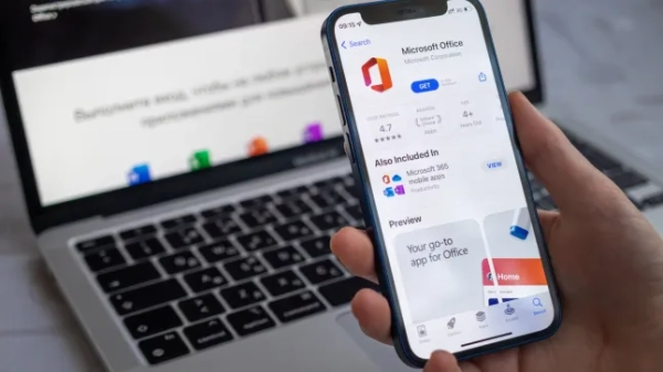 Прем'єр-міністр Данії оголосив, що дітям до 16 років буде заборонено користуватися соціальними мережами без дозволу батьків. Людина тримає смартфон з Microsoft Office на екрані та ноутбук на столі на задньому плані
