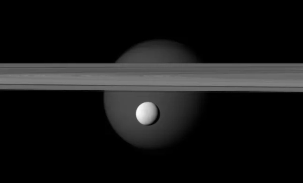 Яскраво відбиваючий супутник Енцелад з'являється перед кільцями Сатурна, а більший супутник Титан маячить удалині. (Фото: Universal History Archive/Universal Images Group via Getty Images)