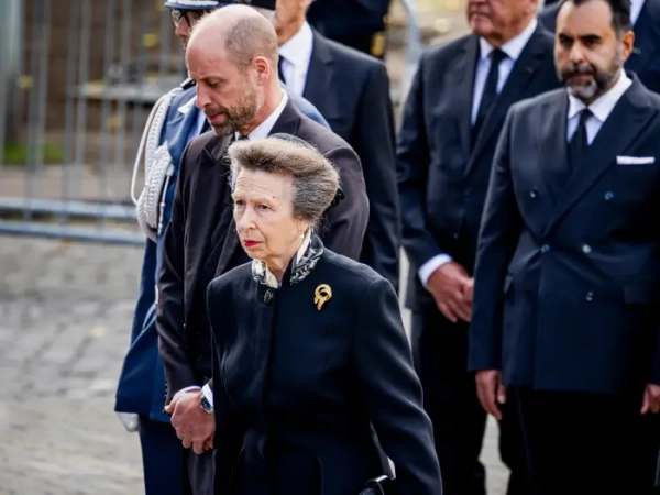 Princess Anne and Prince William walk with formally dressed attendees in a solemn outdoor procession.
