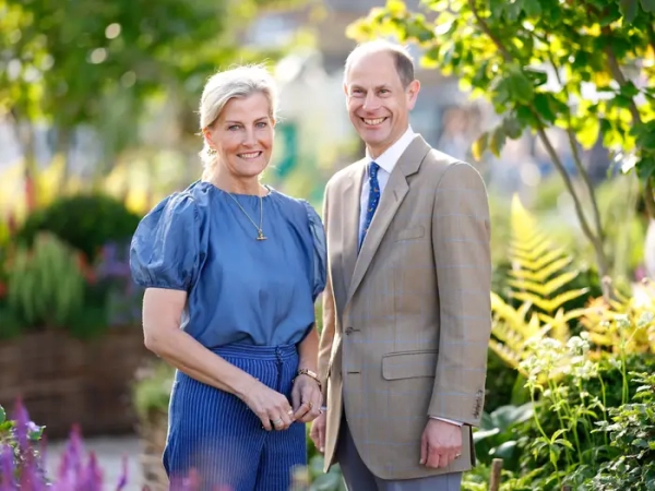 Sophie, Duchess of Edinburgh, and Prince Edward stand together in a sunlit garden with greenery and flowers.