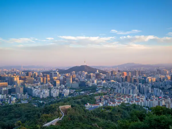 Пейзаж Сеула на заході сонця з вежею N Seoul Tower, що височіє над центральним пагорбом над щільними висотними будівлями.