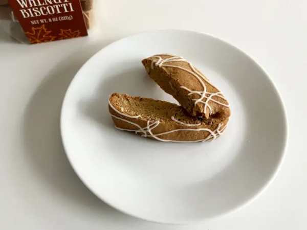 Міні-біскоті з кленом та волоським горіхом від Trader Joe's на білій тарілці поруч із пластиковою коробкою печива.