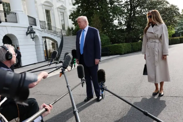 Дональд Трамп говорить до преси, а Меланія Трамп стоїть на задньому плані.