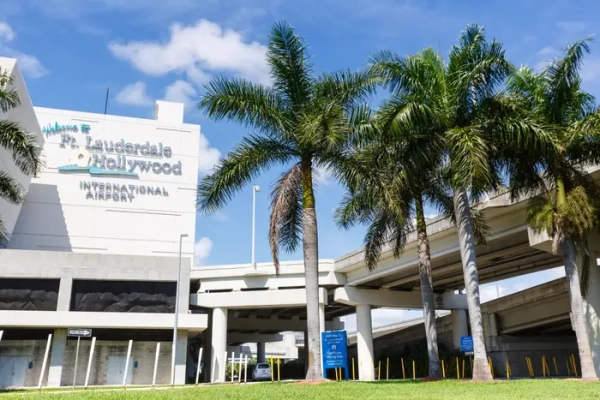 Fort Lauderdale-Hollywood International Airport exterior with palm trees, elevated roadways, and a blue sky.