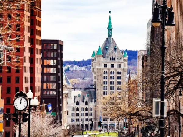Downtown Albany street view frames SUNY Plaza’s green-roofed tower between brick buildings and bare trees.