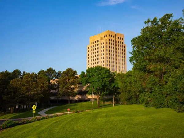 North Dakota State Capitol tower rises above green lawns and trees under a clear blue sky.