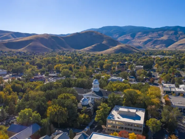 Aerial view of the Nevada State Capitol amid trees with dry mountains beyond.