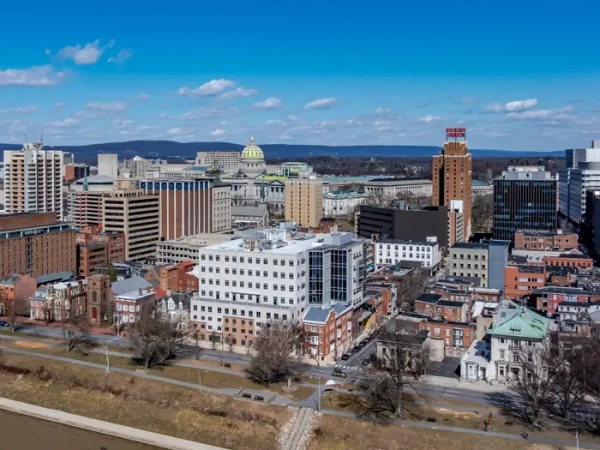 Downtown Harrisburg skyline with Pennsylvania State Capitol dome and riverfront buildings under a blue sky.