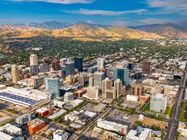 Downtown Salt Lake City skyline spreads toward the Wasatch Mountains under a partly cloudy blue sky.