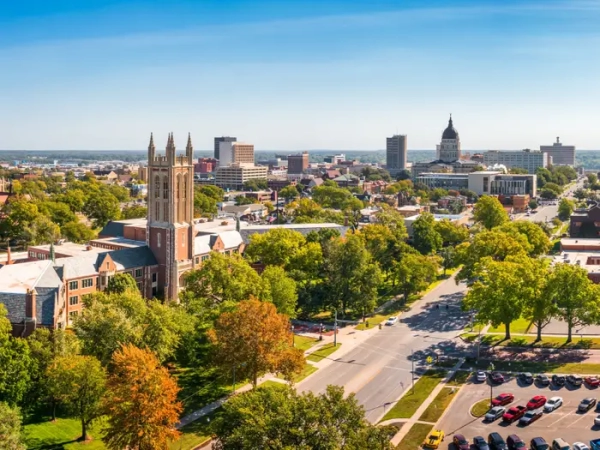 Downtown Topeka skyline with the Kansas State Capitol dome, church towers, tree-lined streets, and parked cars.
