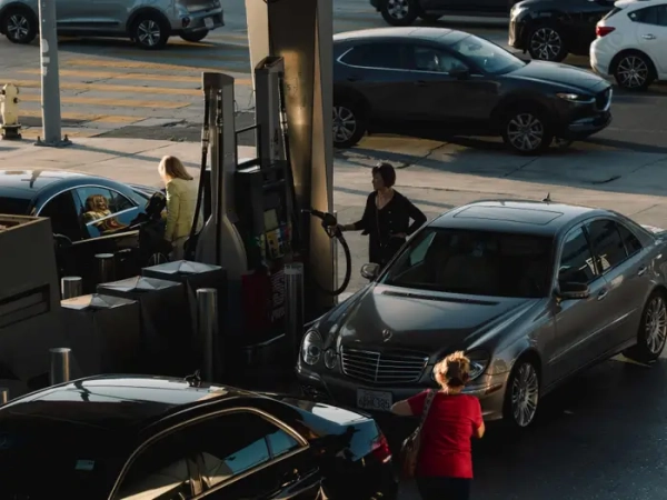 Several people fill up their sedans at a gas station.